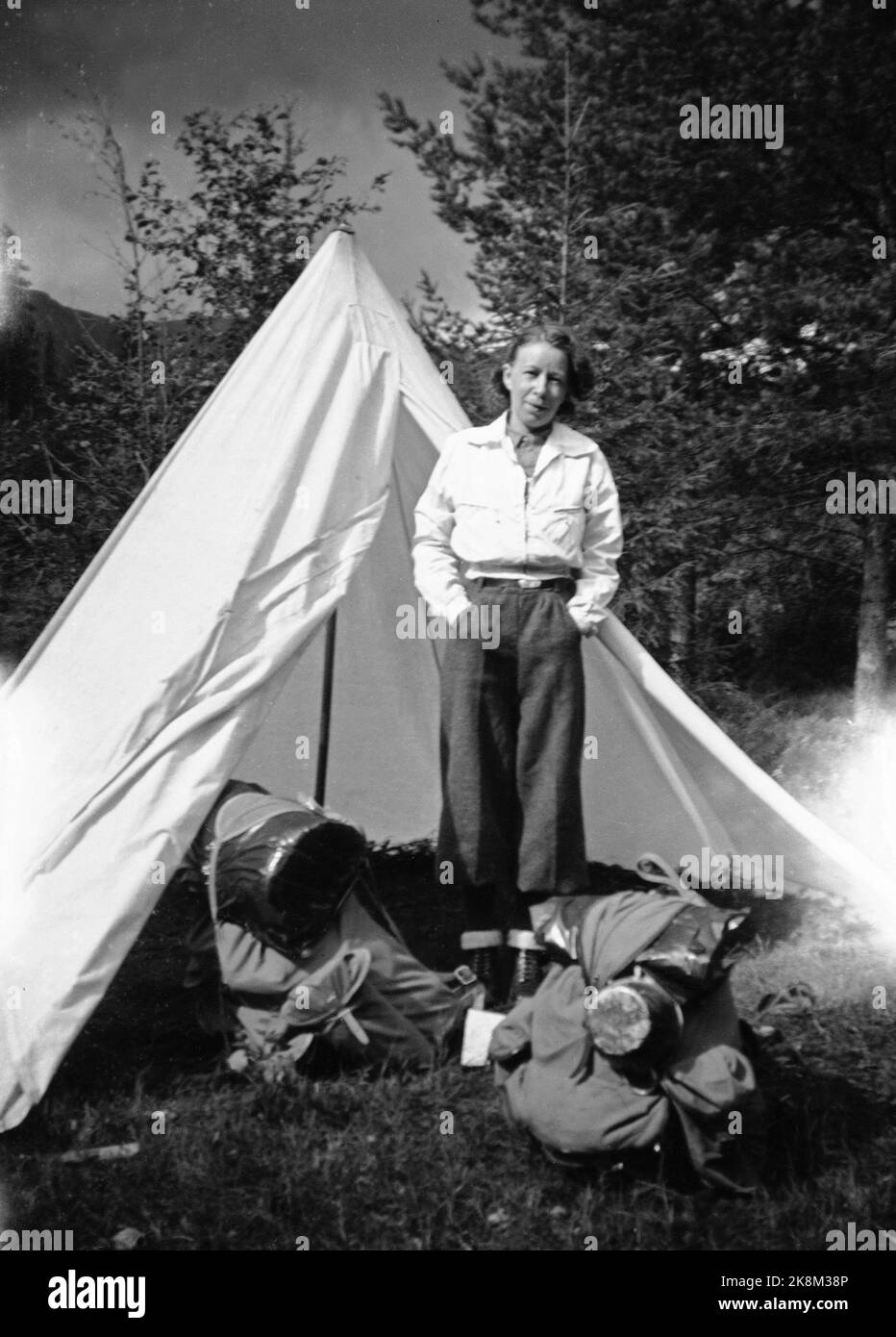 Norwegen, Sommer 1943 Alltag während des Krieges. Reisegenehmigungen waren während des Zweiten Weltkriegs schwierig zu erreichen, weshalb viele sich für eine Radtour entschieden. Ein junges Paar beschäftigte sich mit der Strecke Oslo/Ålesund. Frau in langen Hosen und weißer Jacke vor weißen, speienden Zelten. Im Vordergrund Rucksäcke, die alles enthalten, was sie auf der Reise brauchen können. Foto: NTB Stockfoto