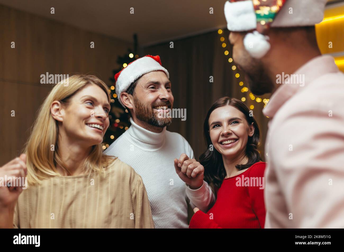 Neujahrsparty verschiedener verwitweter Freunde, Männer und Frauen tanzen aus nächster Nähe, lächeln fröhlich und umarmen das neue Jahr im Wohnzimmer in der Nähe des Weihnachtsbaums. Stockfoto