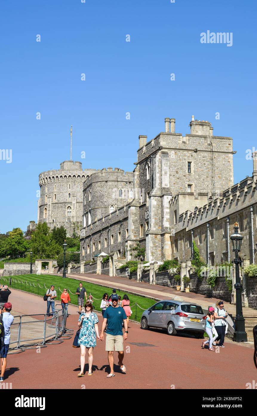 Eine vertikale Aufnahme von Menschen, die auf einem Bürgersteig mit einem Park und dem Windsor Castle Gebäude im Hintergrund spazieren gehen. Stockfoto