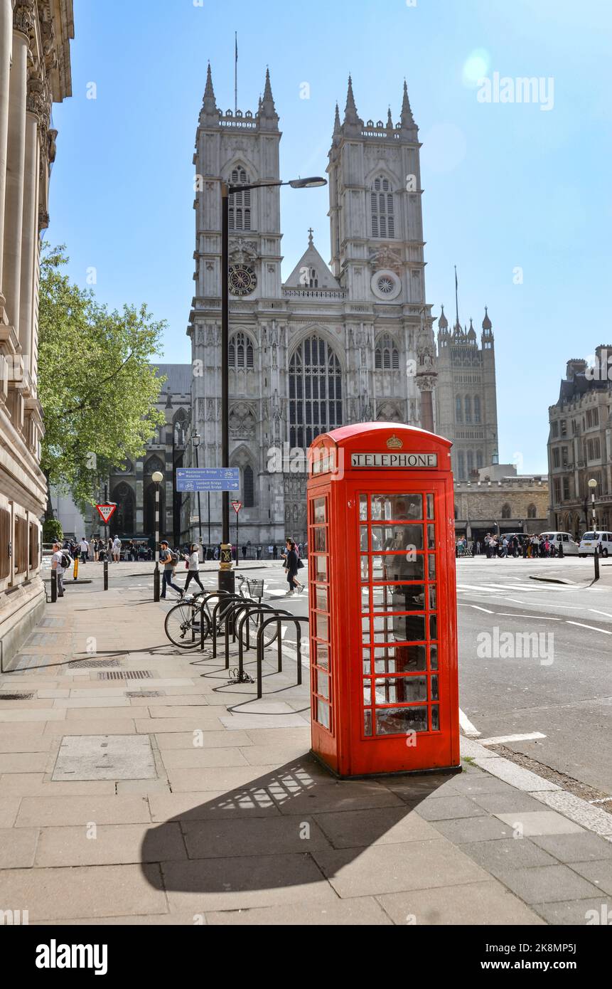 Eine vertikale Aufnahme einer roten Telefonzelle in London, Großbritannien, mit Menschen und dem Westminster Abbey Gebäude im Hintergrund. Stockfoto