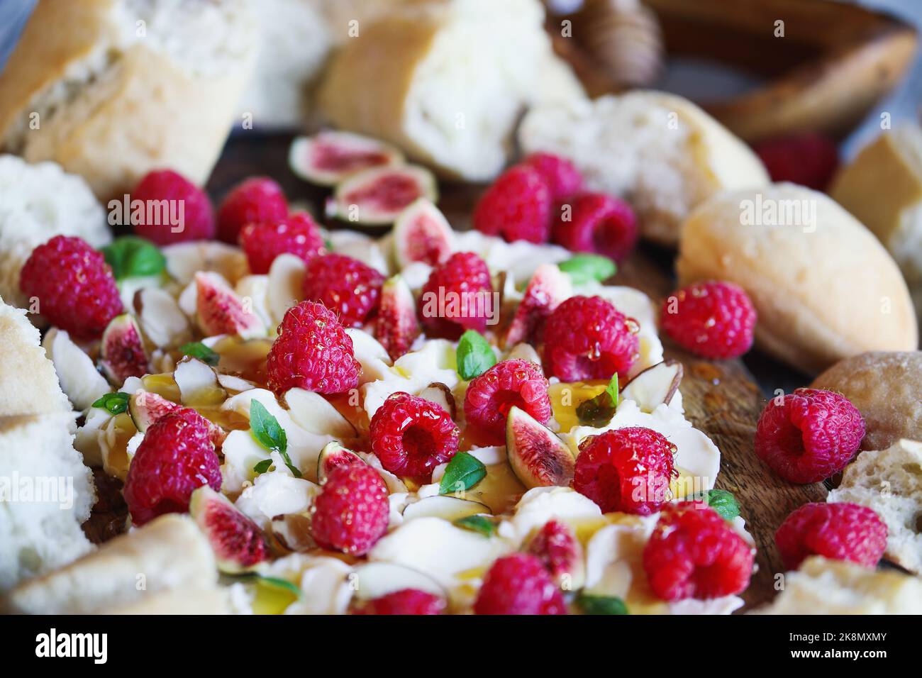 Buttertafel mit frischen Himbeeren, Feigen, in Scheiben geschnittenen Mandeln, Basilikumblättern und mit Honig beträufelt. Selektiver Fokus mit unscharfem Hintergrund. Stockfoto