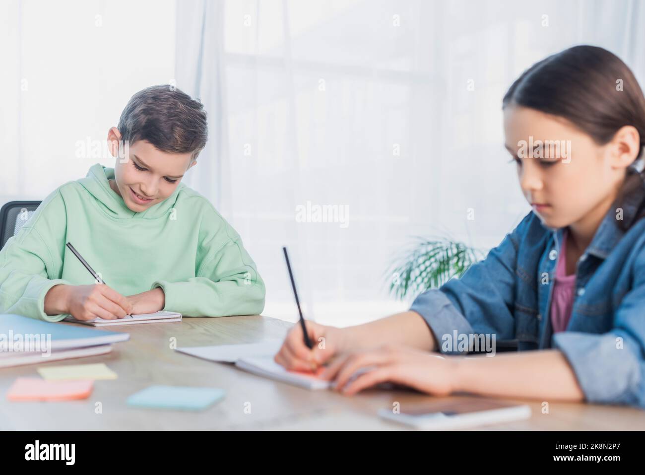 Jugendliche, die in Notizbüchern schreiben, während sie Hausaufgaben auf unscharfem Vordergrundbild machen Stockfoto