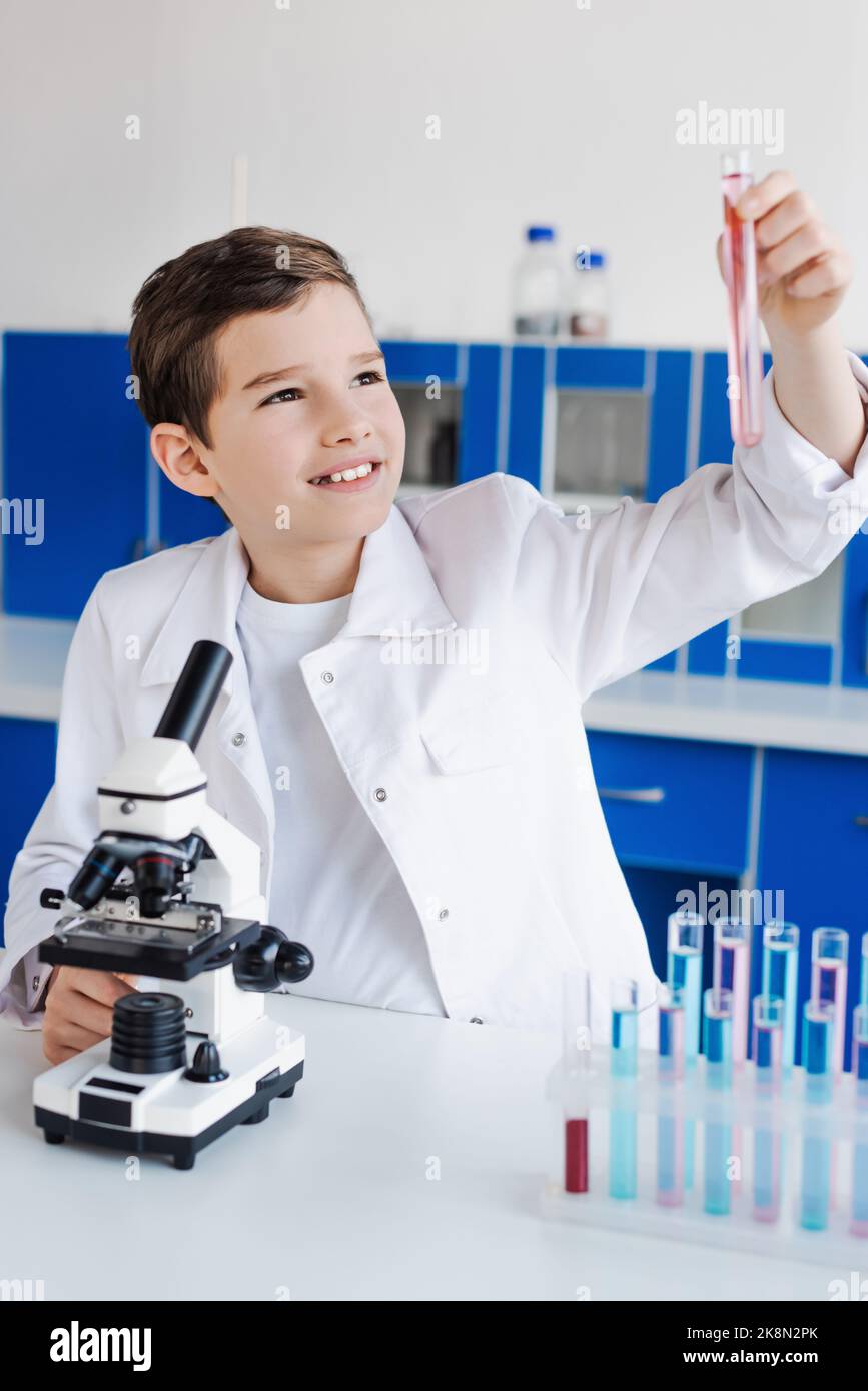 Glücklicher Junge, der in der Nähe des Mikroskops in einem chemischen Labor ein Reagenzglas ansieht, Stockbild Stockfoto