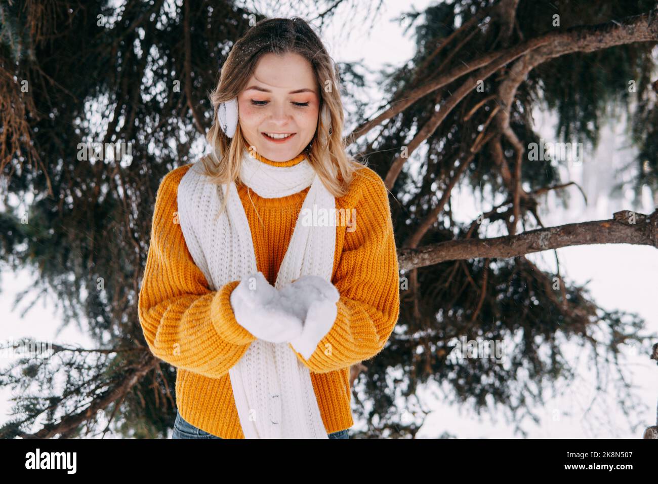 Teen blond in einem gelben Pullover draußen im Winter. Ein Teenager-Mädchen auf einem Spaziergang in Winterkleidung in einem verschneiten Wald. Stockfoto