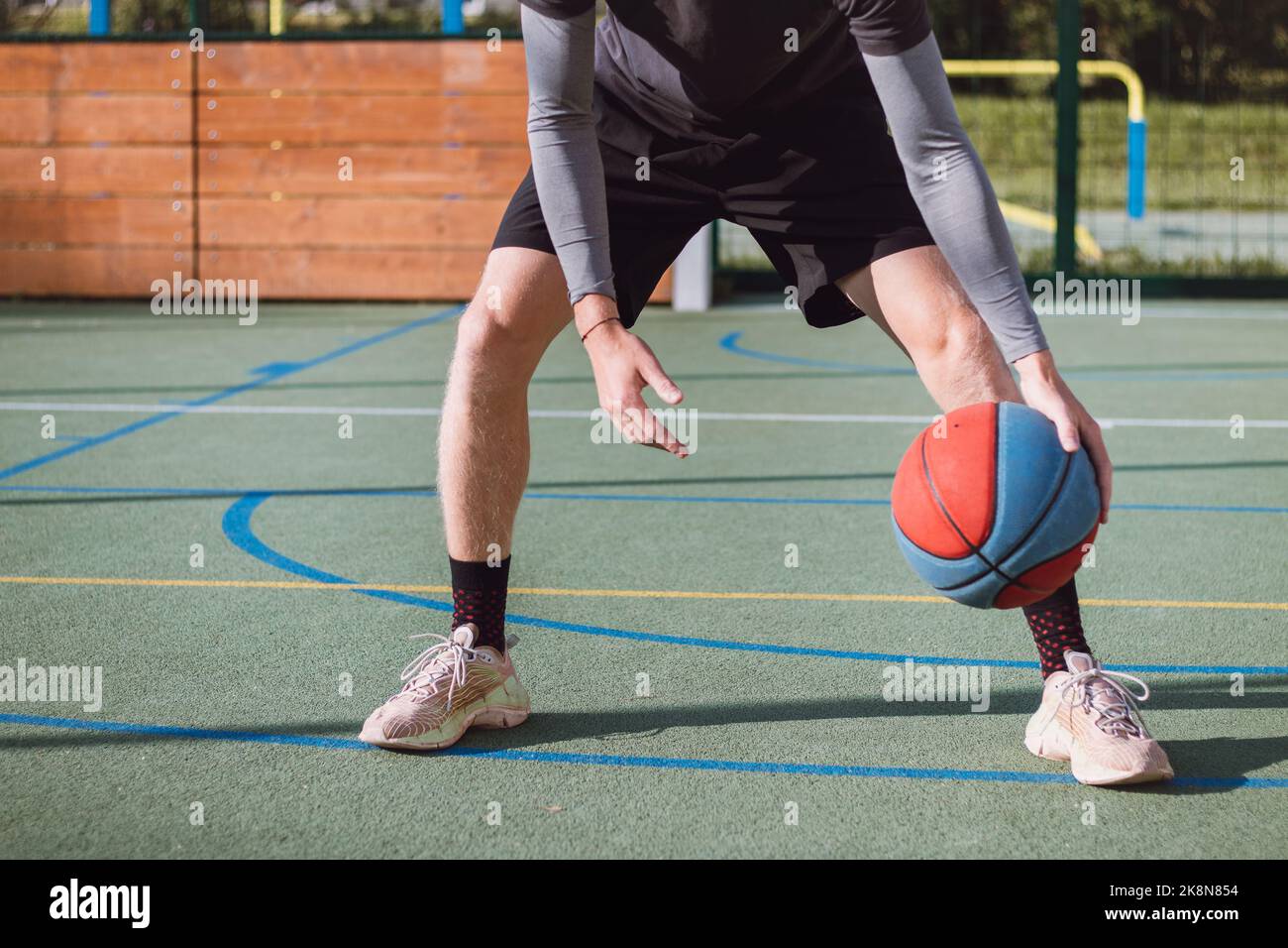 Das junge Talent übt das Dribbeln des Basketballs unter seine Füße und verbessert seine Hand-, Körper- und Fußkoordination. Basketballspiel. Lernen des Tricks, Stockfoto