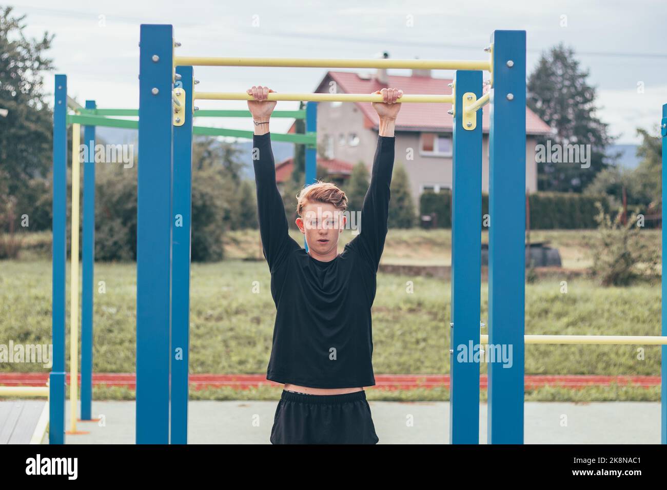 Der zielorientierte blonde Junge baut im Sommer die Kraft seines eigenen Körpers auf dem Trainingsfeld auf. Training von Trizeps, Bizeps, Schultern und Bauch. Stockfoto