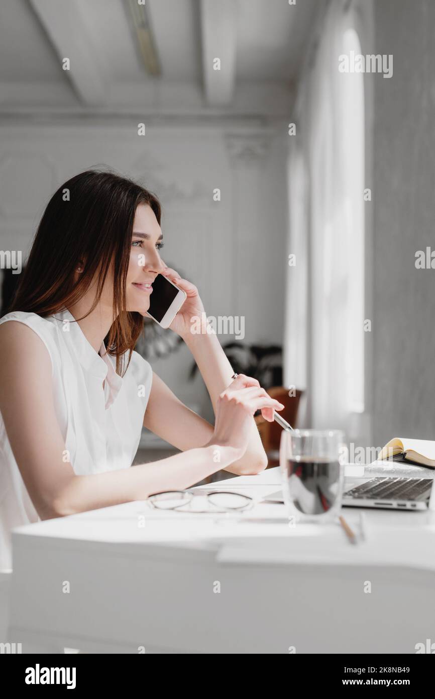 Seitenansicht einer Geschäftsfrau, die am Schreibtisch sitzt und in einem modernen Büro ein Smartphone benutzt. Stockfoto