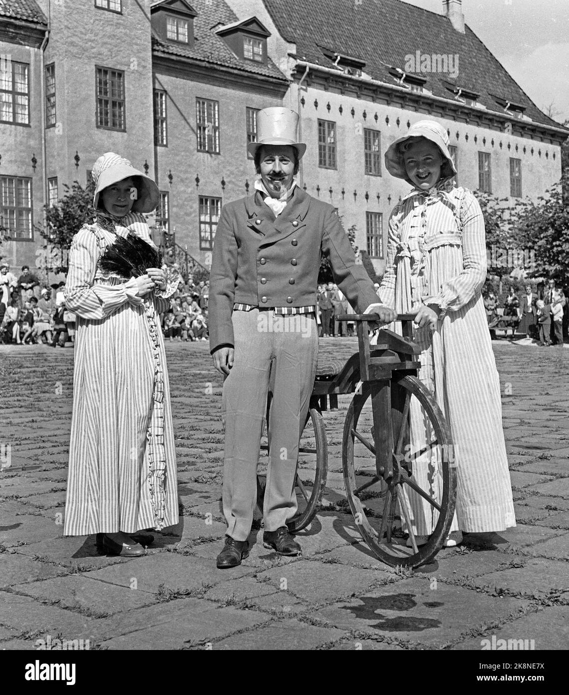 Bygdøy 19570825 Parade von alten Fahrrädern im Volksmuseum. Mann mit Zahnseide Hut und moderne Kleidung und alte Fahrrad mit zwei Frauen, modisch mit langen Kleidern und Küssen gekleidet. Foto: Jan Nordby / NTB / NTB Stockfoto