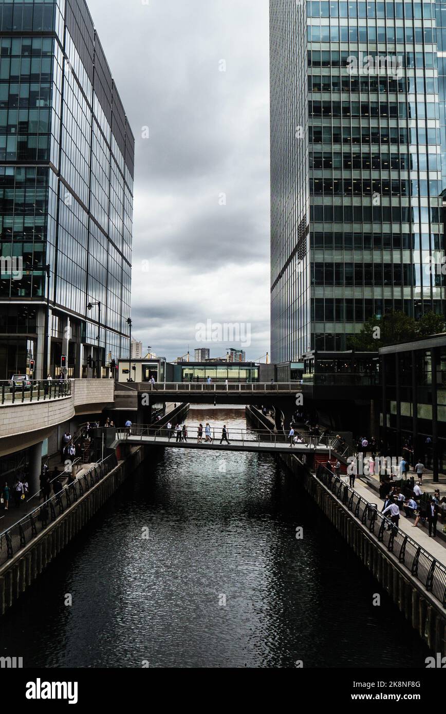 Eine vertikale Aufnahme von zwei gläsernen Wolkenkratzern in London, Großbritannien, mit Menschen auf den Straßen, einem Wasserkanal und einer Brücke. Stockfoto