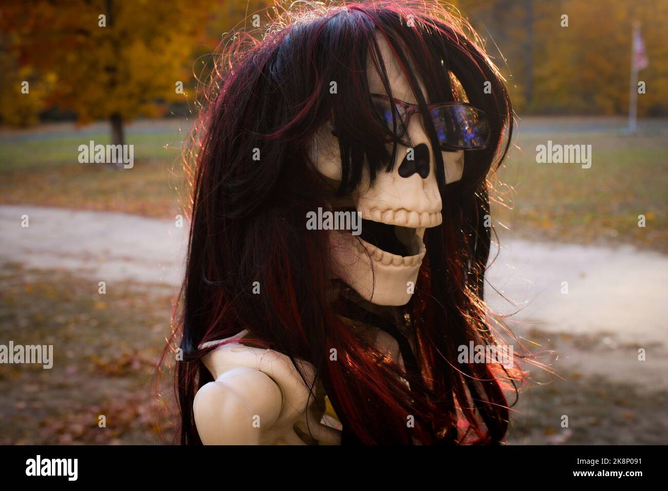 Aus der Nähe eines weiblichen Skeletts auf einem Motorrad mit schönen Herbstfarben und Flagge im Hintergrund sitzen Stockfoto