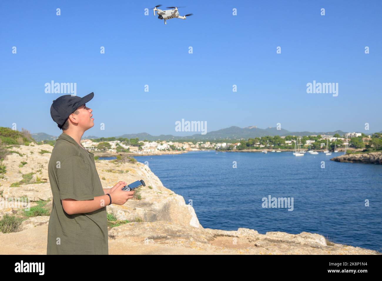 Happy teen boy, fliegende Drohne an der mittelmeerküste, gegen blauen Himmel während sonnigen Tages Spanien, Balearen Stockfoto