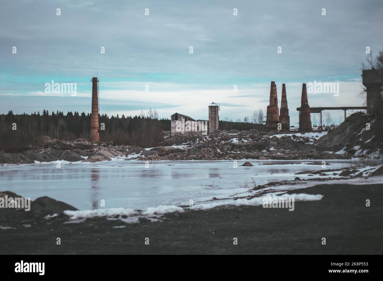 Verlassene zerstörte Fabrik vor dem Wald gefrorenen Fluss mit Eis und Frost im Winter bedeckt Stockfoto