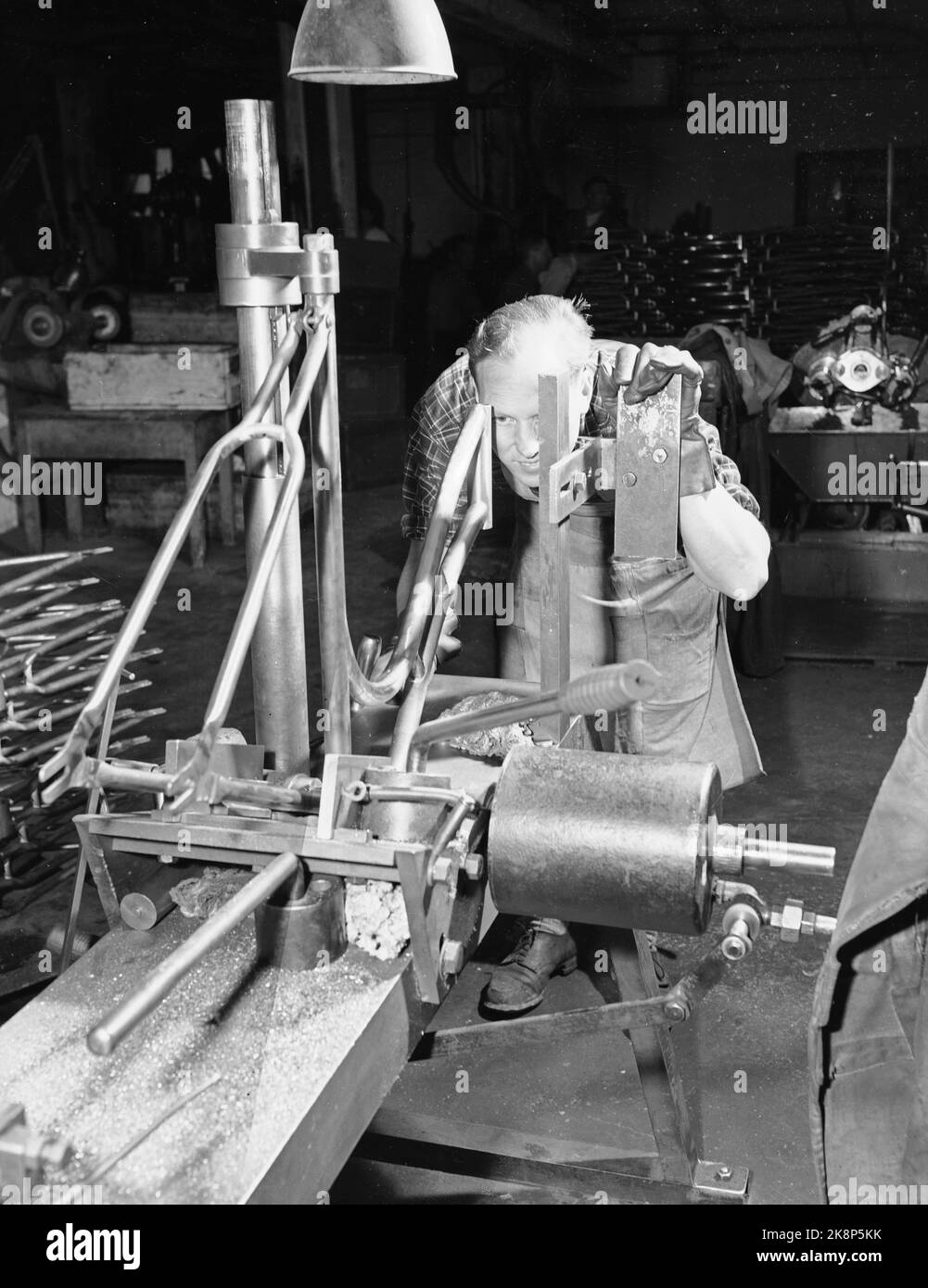Sandnes 19490415. I BÅS MED 75 000 SYKLER. Firmaet Jonas Øglænd i Sandnes, Rogaland ble grunnlagt i 1868. Øglænd sykkelfabrikk Lager 75,000 sykler årlig, halvparten AV dem settes sammeln her ved fabrikken, den andre halvparten blir soll til forhandlere som selv setter dem sammeln eller bruker dem som reservedeler. I 1932 lanserte de Den beste sykkel - DBS. Fabrikken har ca 400 arbeidere. Det er sehr bei alt arbeid er gjort med presisjon Og nøyaktighet, ellers blir ikke sykkelen god å sykle på. Ihr ser vi Paul Nævland som holder på å kontinentrollere at rammen er helt rett. NOE annett tåles ikke. Stockfoto