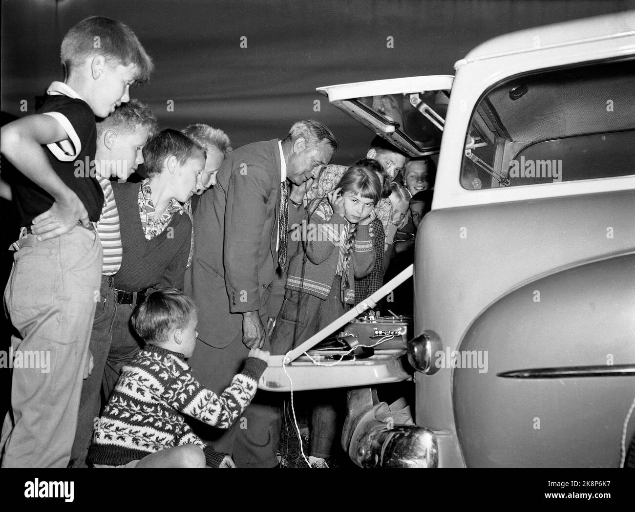 Hokksund 19590709 Norwegian National Broadcasting NRK bei der Arbeit im Feld. Reporter Norland hat eine Gruppe von Zigeunern/Rumänen in Hokksund dazu gebracht, Zigeunershows im Mikrofon zu singen. Kinder dürfen die Aufnahmen von einem Tonbandgerät auf NRK's ​​reporting-Auto hören. Foto: Knoblauch / NTB / NTB Stockfoto