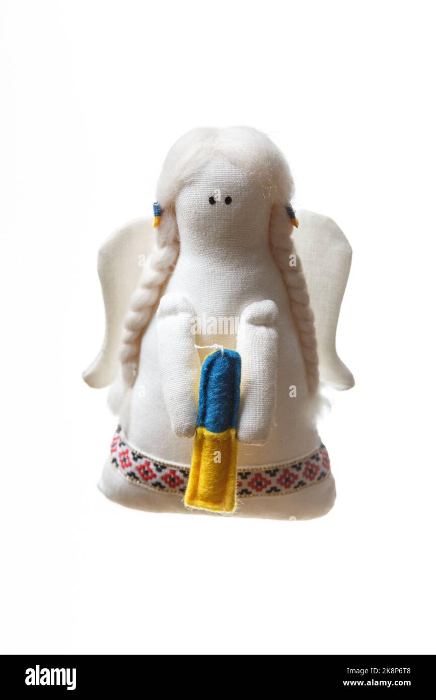 Weißes Stoff weiches Engel Spielzeug mit Flügeln hält eine Kerze mit einer Farbe der ukrainischen Flagge - blau und gelb. Betet für das Konzept der Ukraine Stockfoto