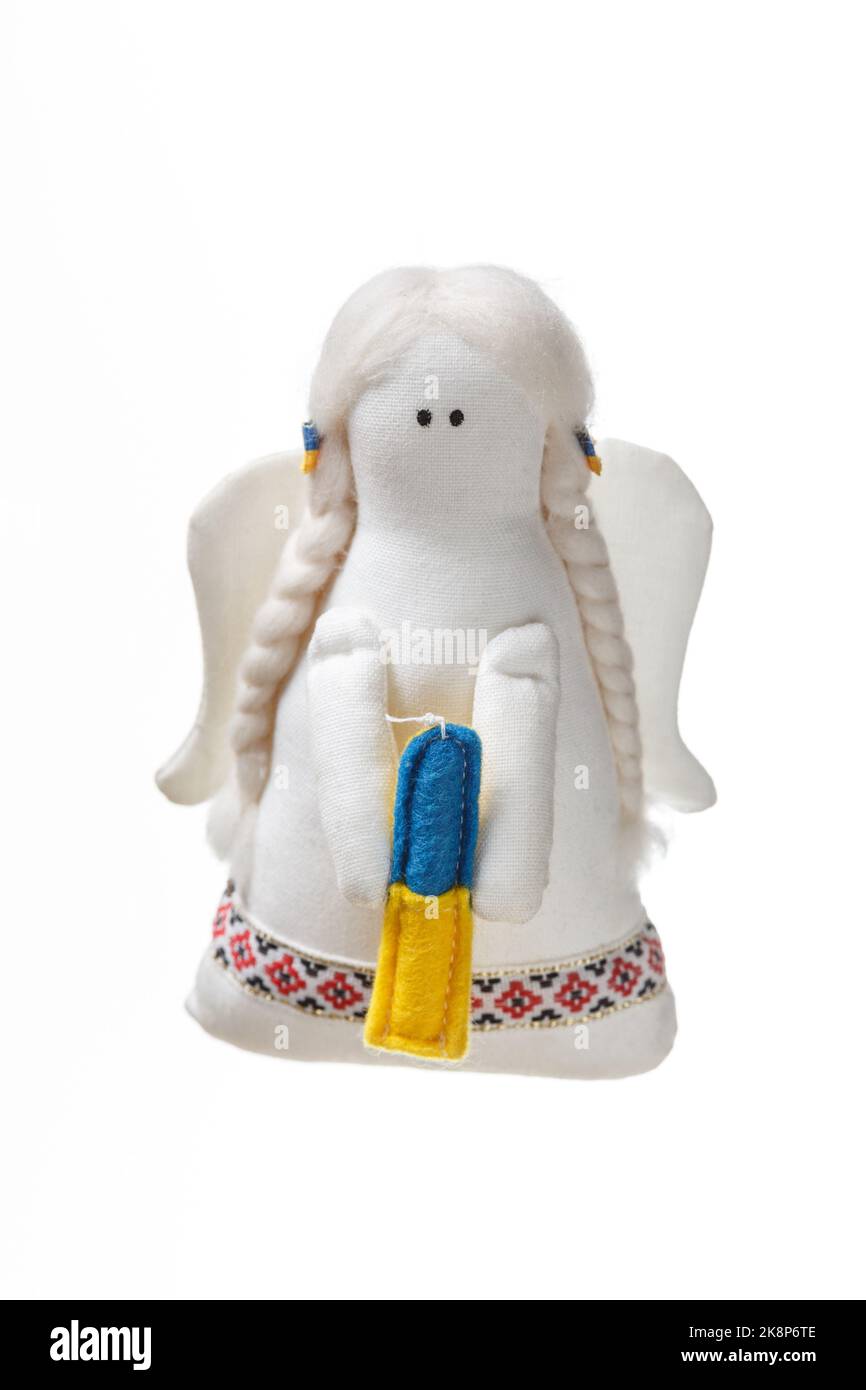 Weißes Stoff weiches Engel Spielzeug mit Flügeln hält eine Kerze mit einer Farbe der ukrainischen Flagge - blau und gelb. Betet für das Konzept der Ukraine Stockfoto