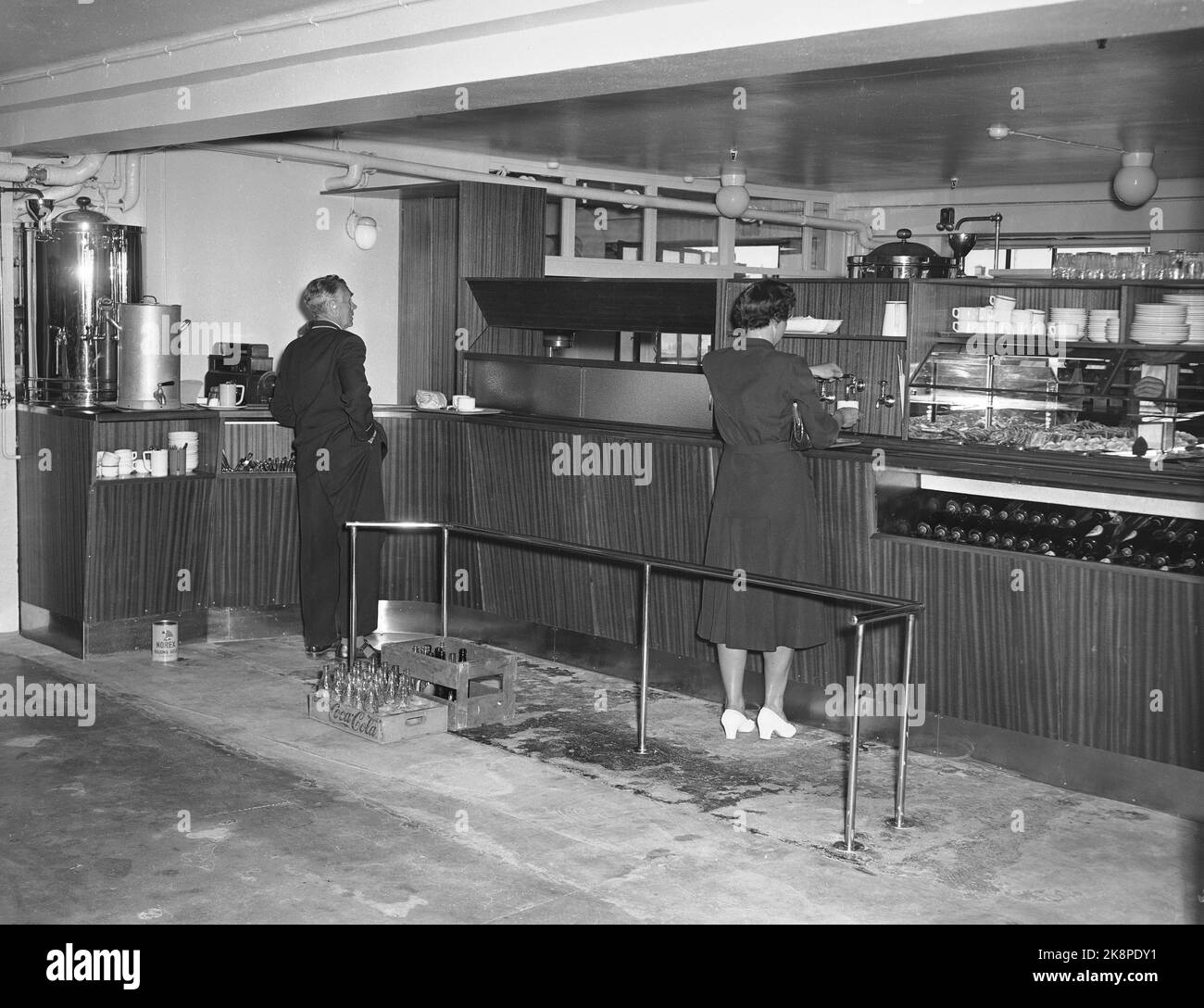 Oslo 19550619. Steen & Strøm. Warenmagazin im Tor 23 von Kongens. Innenmotiv aus Norwegens ältestem großen Magazin. Ein Mann und eine Frau sind am Schalter im Café. Er mit einer Tasse Kaffee, während sie einen an den Wasserhähnen abholt. Beachten Sie die Schachtel mit Cola-Flaschen auf dem Boden. Stockfoto