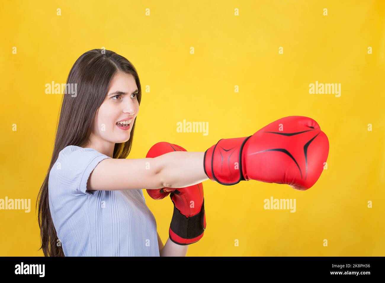 Wütende junge Frau mit roten Boxhandschuhen steht in Kampfposition und sticht mit der Hand. Portrait eines starken und entschlossenen Mädchens, das sich auf den Kampf i vorbereitet hat Stockfoto