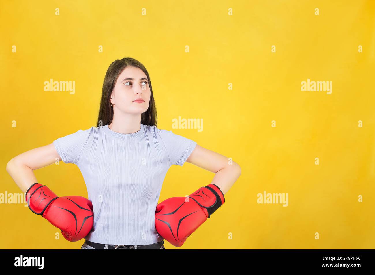 Selbstbewusste junge Frau mit roten Boxhandschuhen steht mit Händen auf den Hüften zur Seite schauen. Portrait von starken und entschlossenen Mädchen isoliert auf gelbem Rücken Stockfoto