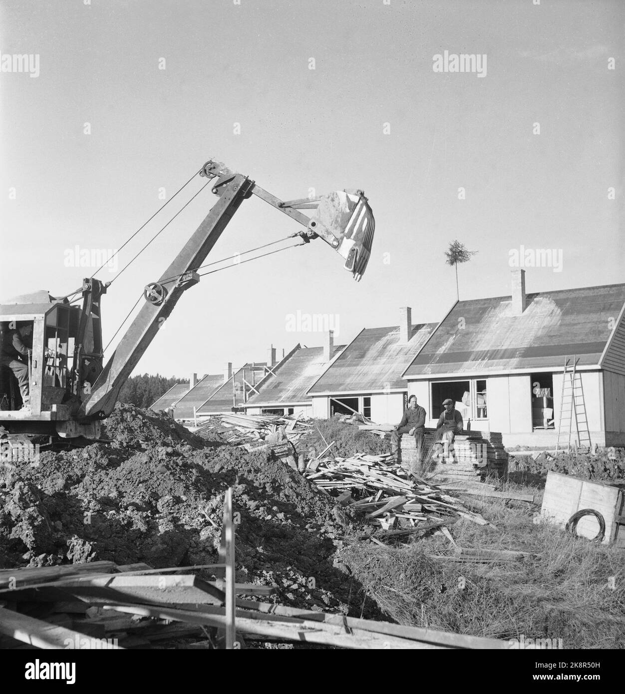 Bærum. Nadderud 1951. Auf Nadderud werden 48 Häuser gebaut. „Es wird von Stadthäusern auf der eineinhalb Etage gesprochen, die nach amerikanischen Prinzipien eingerichtet sind. Jede Wohnung ist in 4 Zimmern und Küchen, mit einer Gesamtfläche von ​​115, neben dem Keller unter der Hälfte des Hauses. Die Miete wird 160.- Kronen pro Monat betragen, kann aber wahrscheinlich reduziert werden. Die Kaution wird auf NOK 7.000 pro Wohnung geschätzt. Hier ist ein alter Bagger vor den Häusern. Foto: Sverre A. Børretzen / NTB Stockfoto