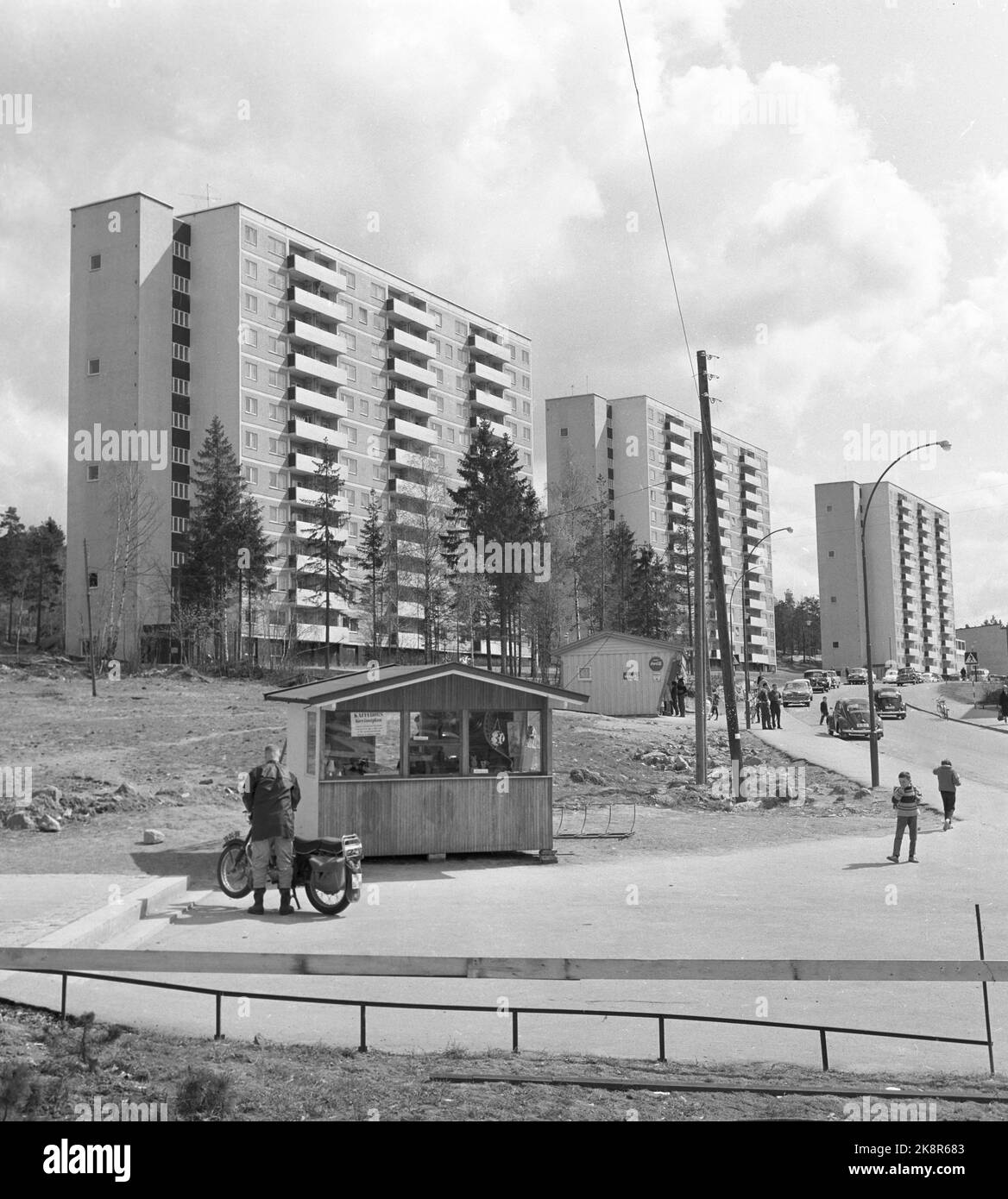 Oslo 19620519: Bøler - Drabantby in Oslo. Hohe Blöcke, mit ein paar geparkten Autos entlang einer Straße. Wagen der Menschen, Blasen. Kinder hängen in der Nähe eines kleinen Kiosk. Mann mit dem Motorrad. Foto: NTB Neuer Scan nicht löschen! Siehe sp0ec1f5 SPBEKEIL Stockfoto