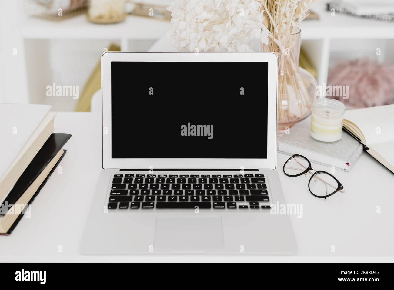 Laptop-Modell mit Büchern, Brillen, Notizbuch, Kerze und Blumen auf weißem Schreibtisch. Stockfoto