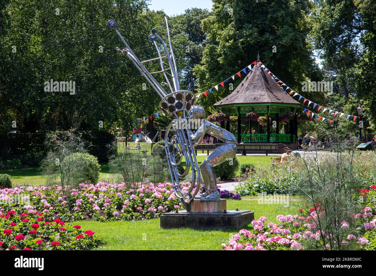 Eine skulpturale Statue eines Kindes, das Noten aus einer Tuba mit dem Bandstand im Garten bläst Stockfoto