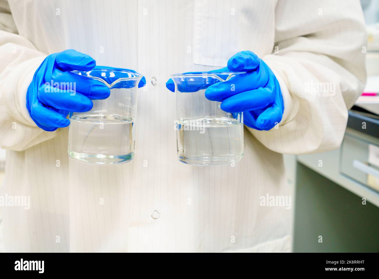 Eine Person in einem Labormantel hält zwei Becher mit klaren Flüssigkeiten Stockfoto