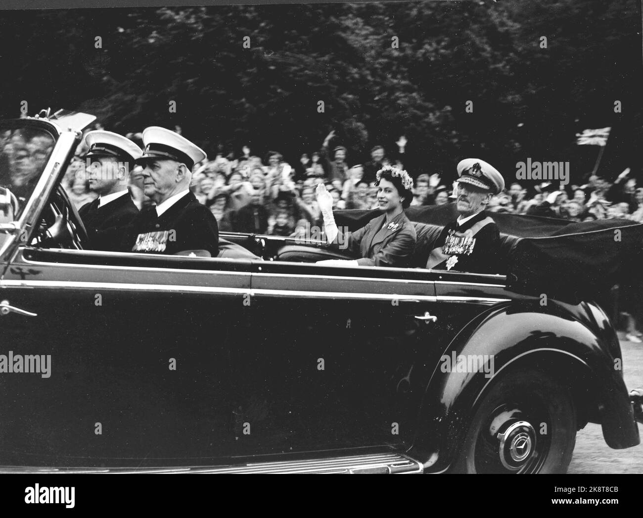 Oslo 19550624. Königin Elisabeth II. Bei einem Staatsbesuch in Norwegen mit ihrem Mann Prinz Philip. Hier sehen wir die königliche Abkürzung in einem offenen Auto mit Königin Elizabeth und König Haakon. Die Königin winkt und lächelt die Menschen an, die gekommen sind, um einen Blick auf sie zu erhaschen. Die Abkürzung wird vom Anlegesteg zum Schloss geführt. Foto: NTB Archive / NTB Stockfoto