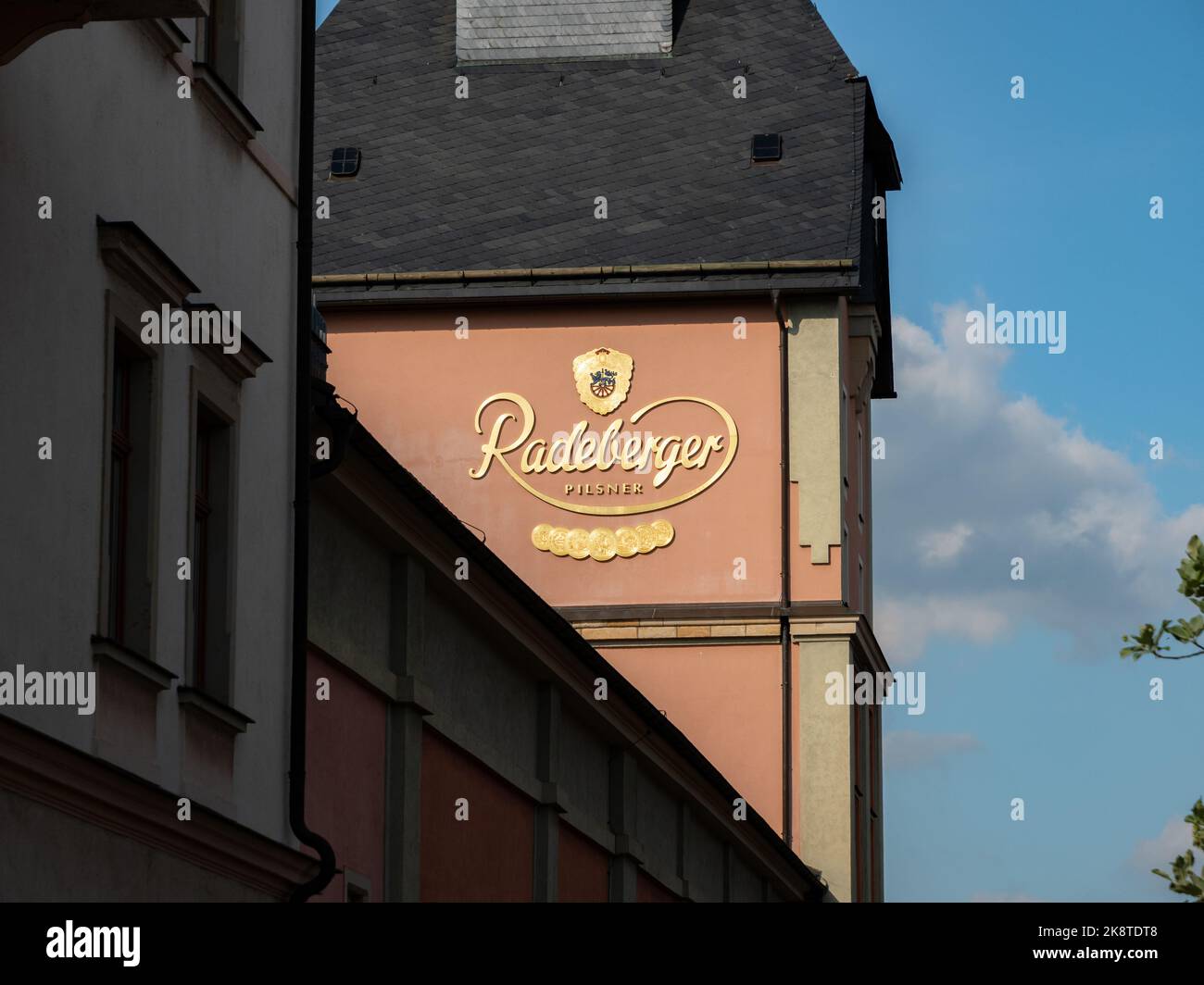 Gebäude der Bierbrauerei Radeberger mit einem großen goldenen Logo an der Fassade. Das Sonnenlicht beleuchtet das Schild an der Außenwand des Unternehmens. Stockfoto