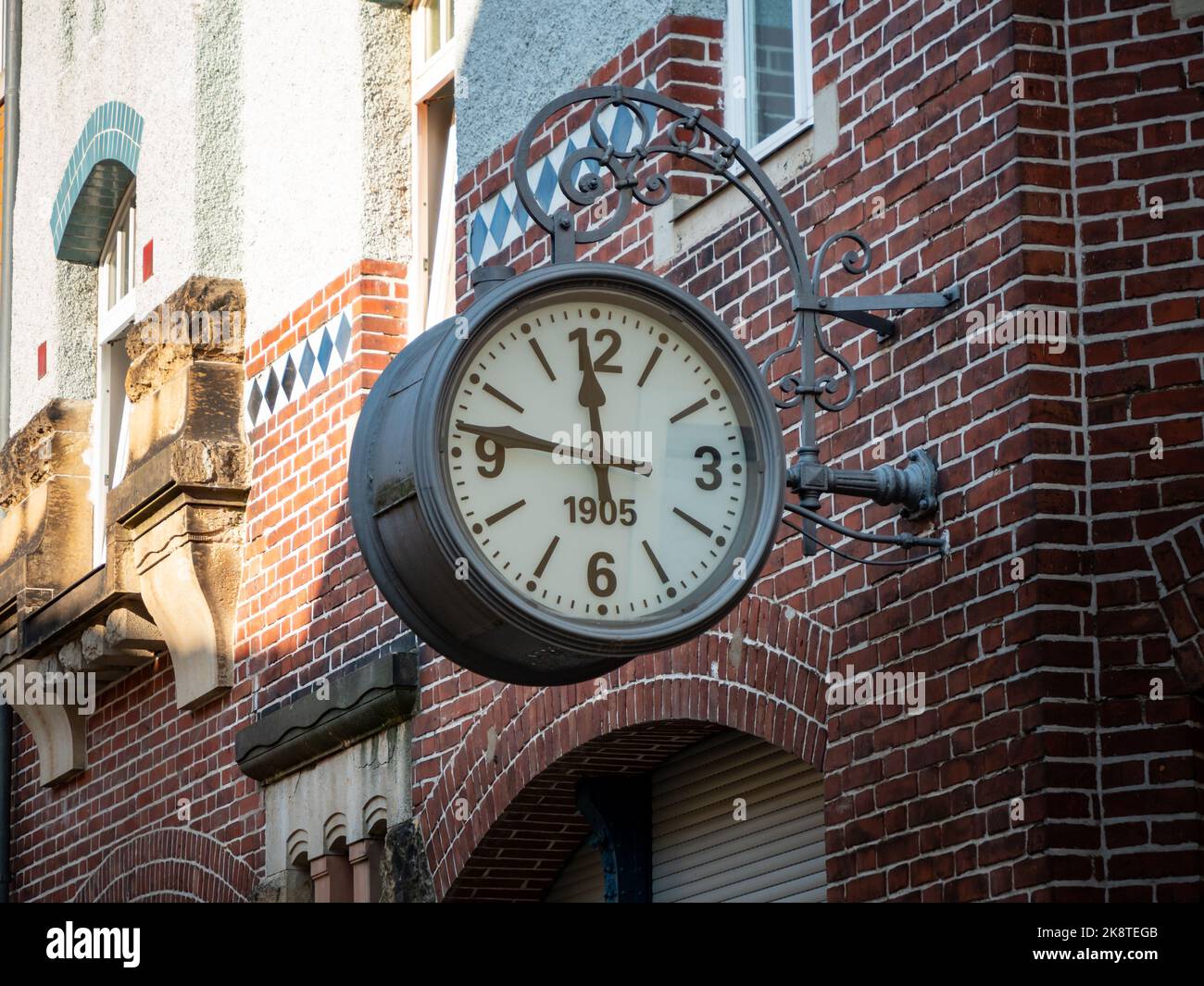 Eine große alte Uhr hängt an der Außenwand eines Gebäudes. Vintage Design-Objekt auf einer roten Ziegelwand. Die alte Stahluhr zeigt die Zeit an. Stockfoto