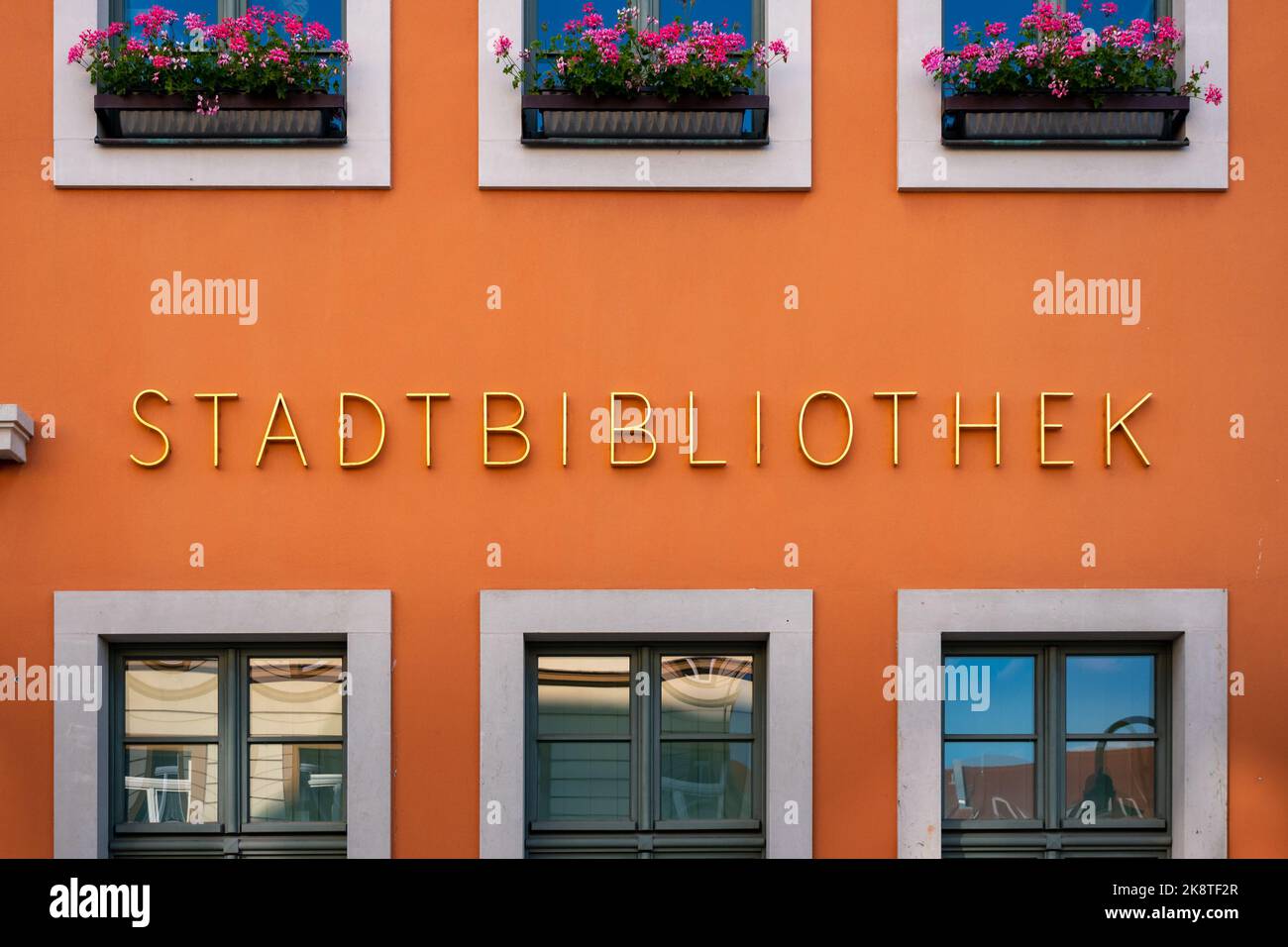 Beschriftung der Stadtbibliothek auf der Außenseite des Gebäudes. Goldene Buchstaben auf einer orangefarbenen Fassade. Ein Service zum Ausleihen von Büchern in einer Stadt. Stockfoto