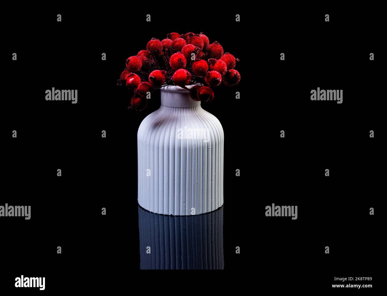 Eine Nahaufnahme von roten Beeren im Eis in einer weißen Vase. Die Porzellanvase hat eine geriffelte Oberfläche. Die Vase mit einem Haufen ist gegen den blsck Rücken isoliert Stockfoto