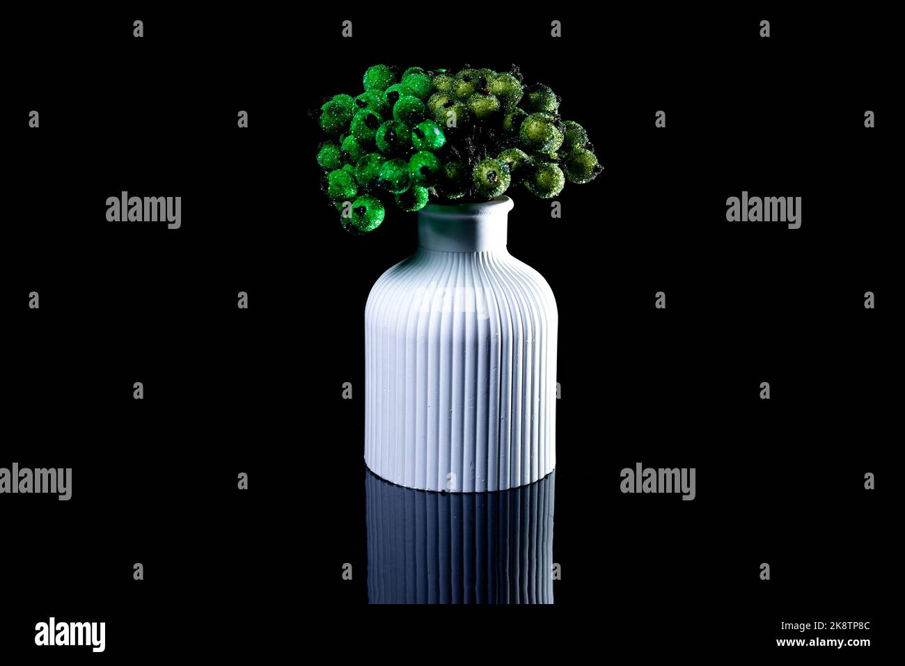 Eine Nahaufnahme von grünen Beeren im Eis in einer weißen Vase. Die Porzellanvase hat eine geriffelte Oberfläche. Die Vase mit einem Bund ist gegen die blsck BA isoliert Stockfoto