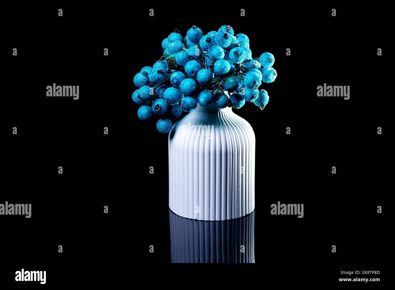 Eine Nahaufnahme von blauen Beeren im Eis in einer weißen Vase. Die Porzellanvase hat eine geriffelte Oberfläche. Die Vase mit einem Haufen ist gegen den blsck Bac isoliert Stockfoto