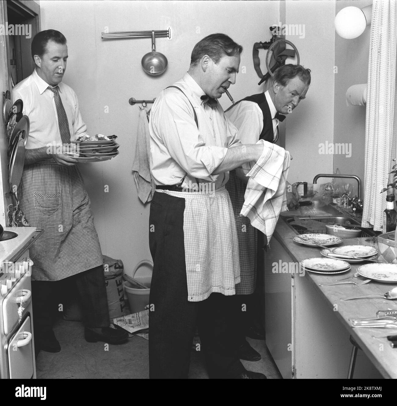 Oslo Weihnachten 1958. Mitglieder von „Press's Lutlag“ haben einen höchst ungewöhnlichen Weihnachtstisch zusammengestellt. Jeder Mann machte sogar das Recht, das er bevorzugen würde. Der Weihnachtstisch wurde in Lijordet mit der Familie Leif Borthen arrangiert. Nach dem Weihnachtstisch musste hier das Geschirr eingenommen werden. Journalist Arne Hestenes, Redakteur per Monsen mit Zigarre und Schauspieler Ola Isene. Alle mit Schürze. Zigarre rauchen. Foto: Aage Storløkken Current / NTB Stockfoto