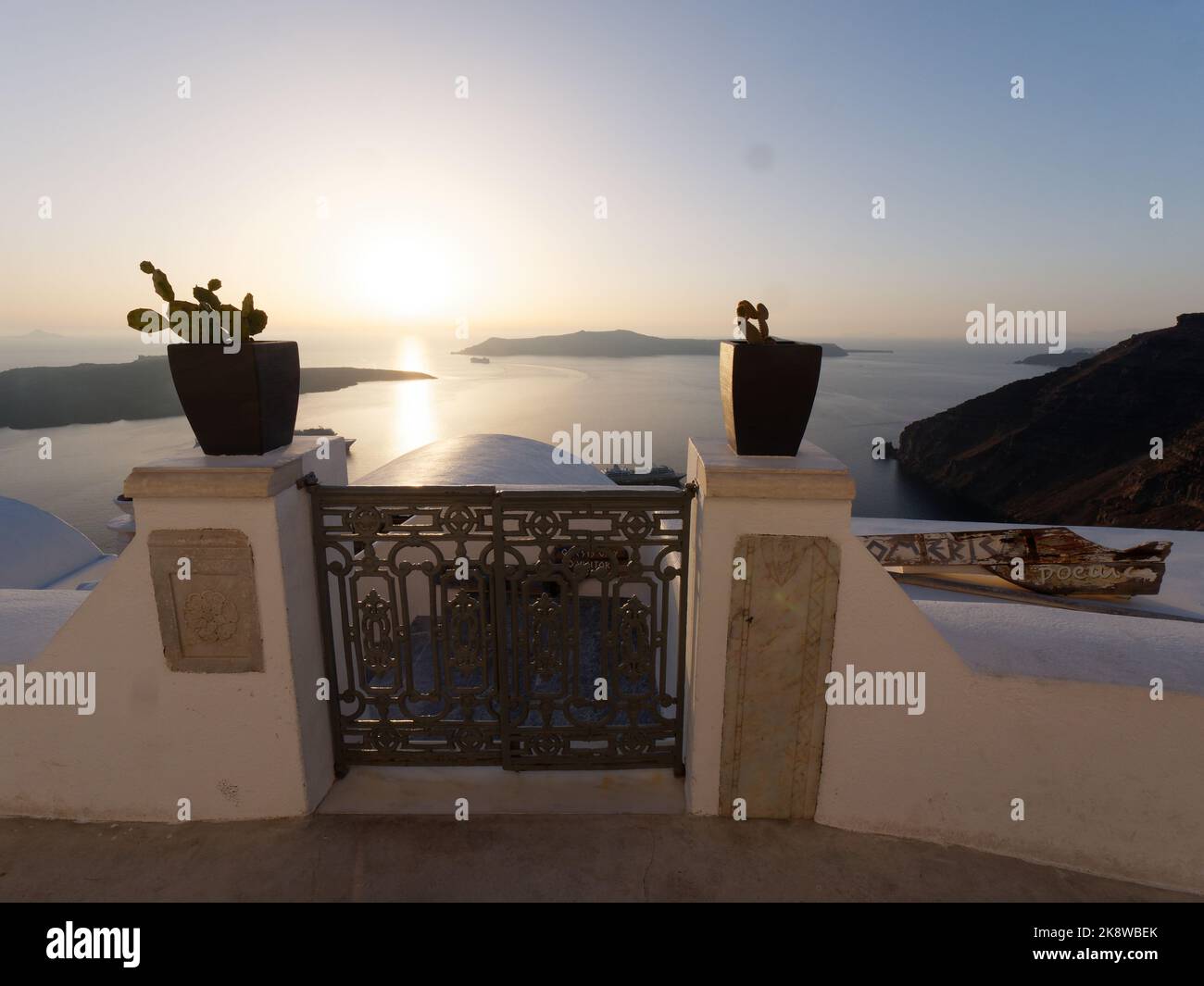 Blick auf Firostefani über die Caldera bei Sonnenuntergang. Griechische Kykladen-Insel Santorin in der Ägäis. Blumentöpfe mit Kakteen im Vordergrund Stockfoto
