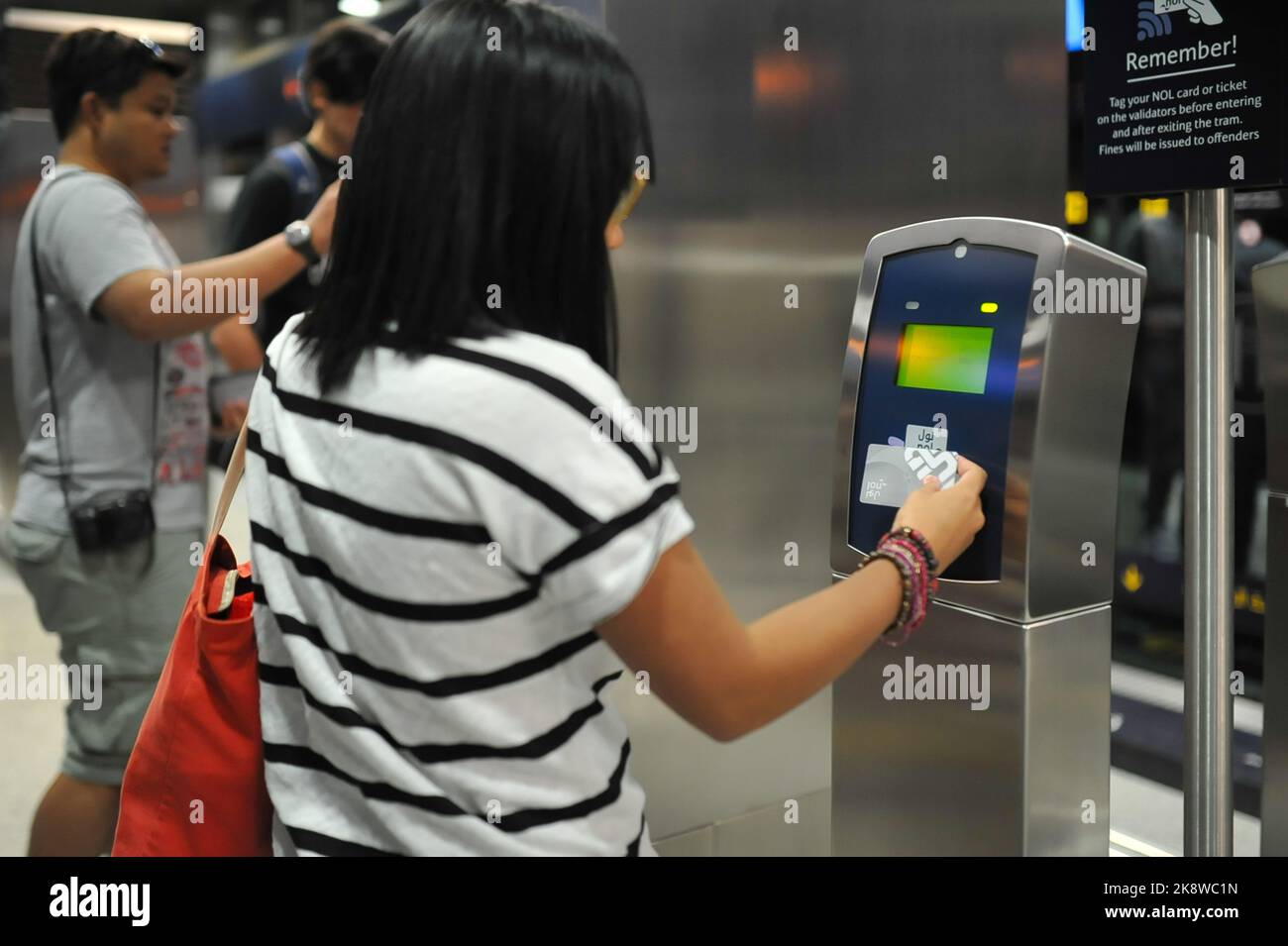 Weibliche Pendler tippt die silberne Dubai Metro Nol Card auf den Leser der Straßenbahnhaltestelle, um den Zug zu fahren. Effiziente öffentliche Verkehrsmittel in der modernen Stadt im Nahen Osten. Stockfoto