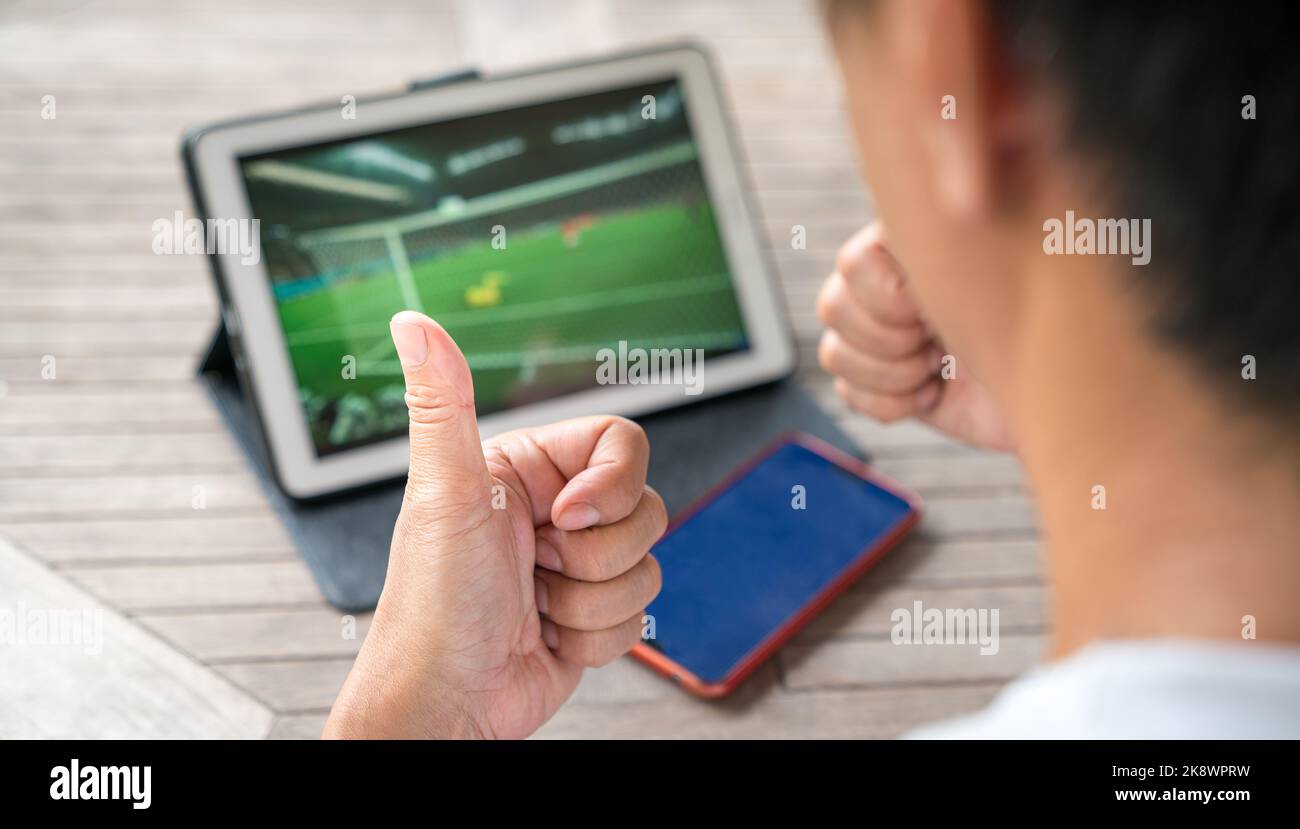 Mann mit Daumen nach oben, während er Fußballsportspiele auf einem digitalen Tablet ansieht. Live-Stream oder Sport Online-Konzept. Stockfoto