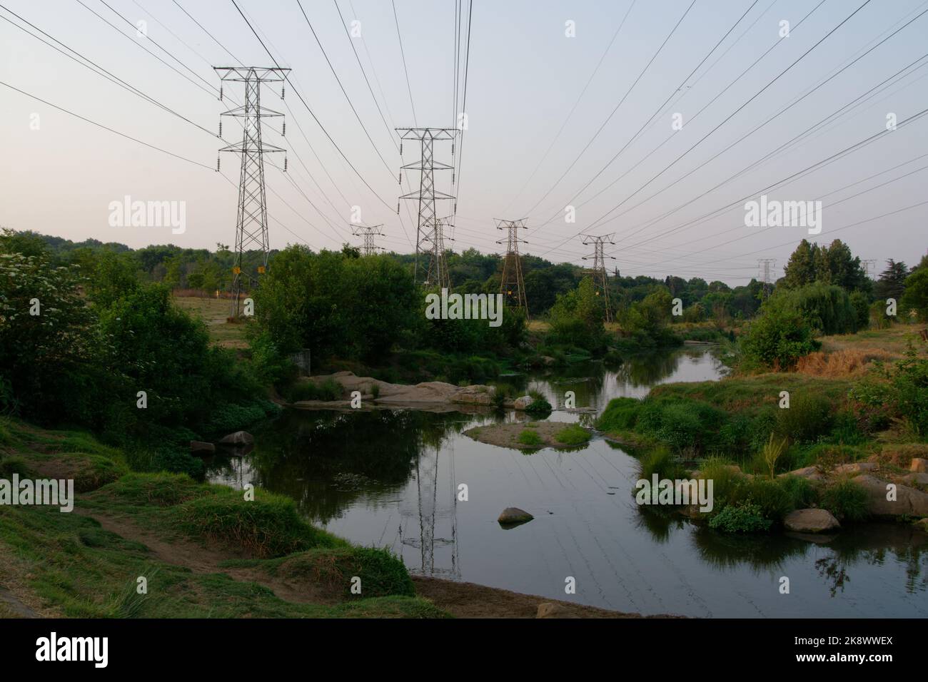 Eine angenehme Flusslandschaft, die von großen elektrischen Masten und Hochspannungsfreileitungen überschattet wird. Stockfoto