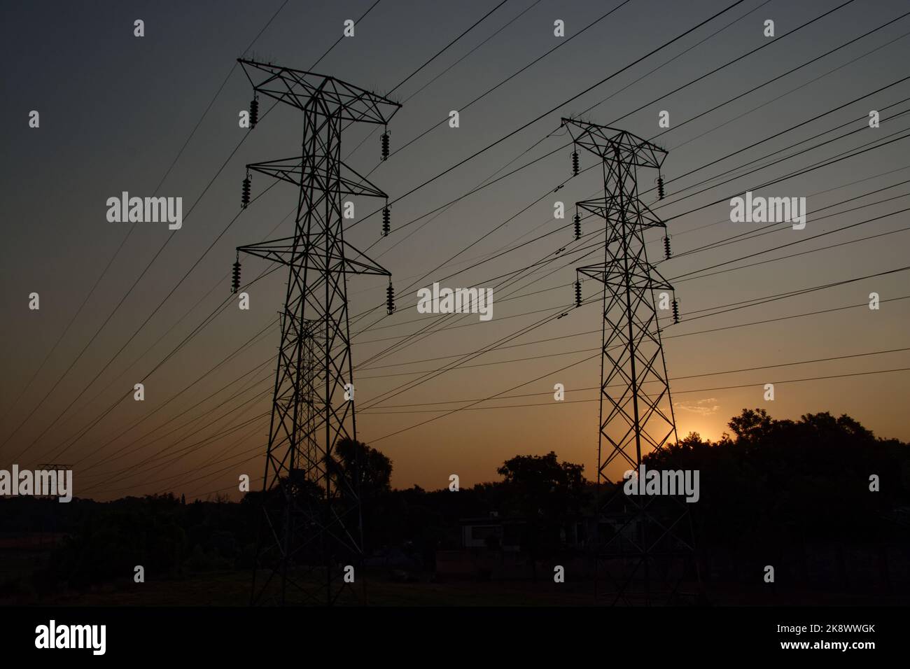 Zwei Strommasten von Electrical Power wurden gegen den goldenen Abendhimmel silhouettiert. In ländlicher Umgebung. Stockfoto