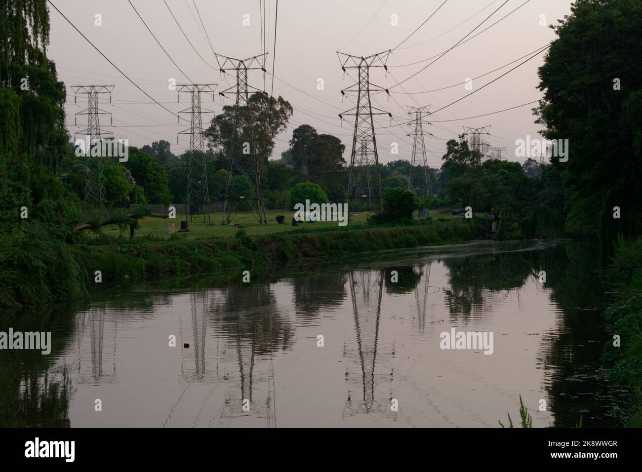 Die elektrischen Oberleitungen wurden auf Pylonen getragen, die einen ruhigen und friedlichen Fluss überquerten. Die Kabel sind über dem Kopf und spiegeln sich im Fluss wider. Sehr friedlich. Stockfoto