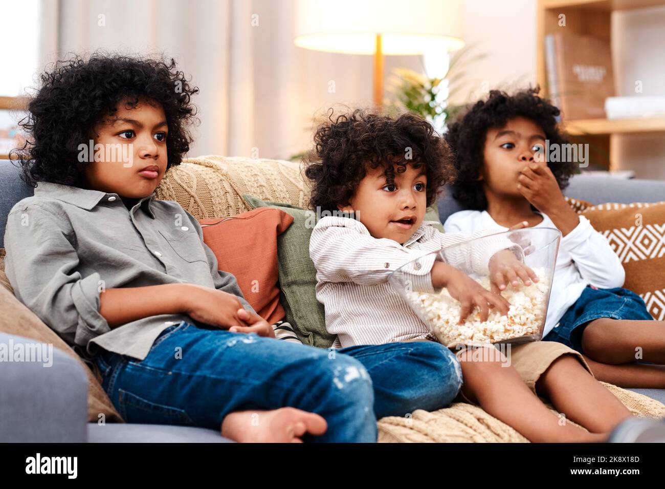 Dieser Film hält sie alle in Spannung. Drei entzückende kleine Jungen essen Popcorn und sehen Filme zusammen zu Hause. Stockfoto