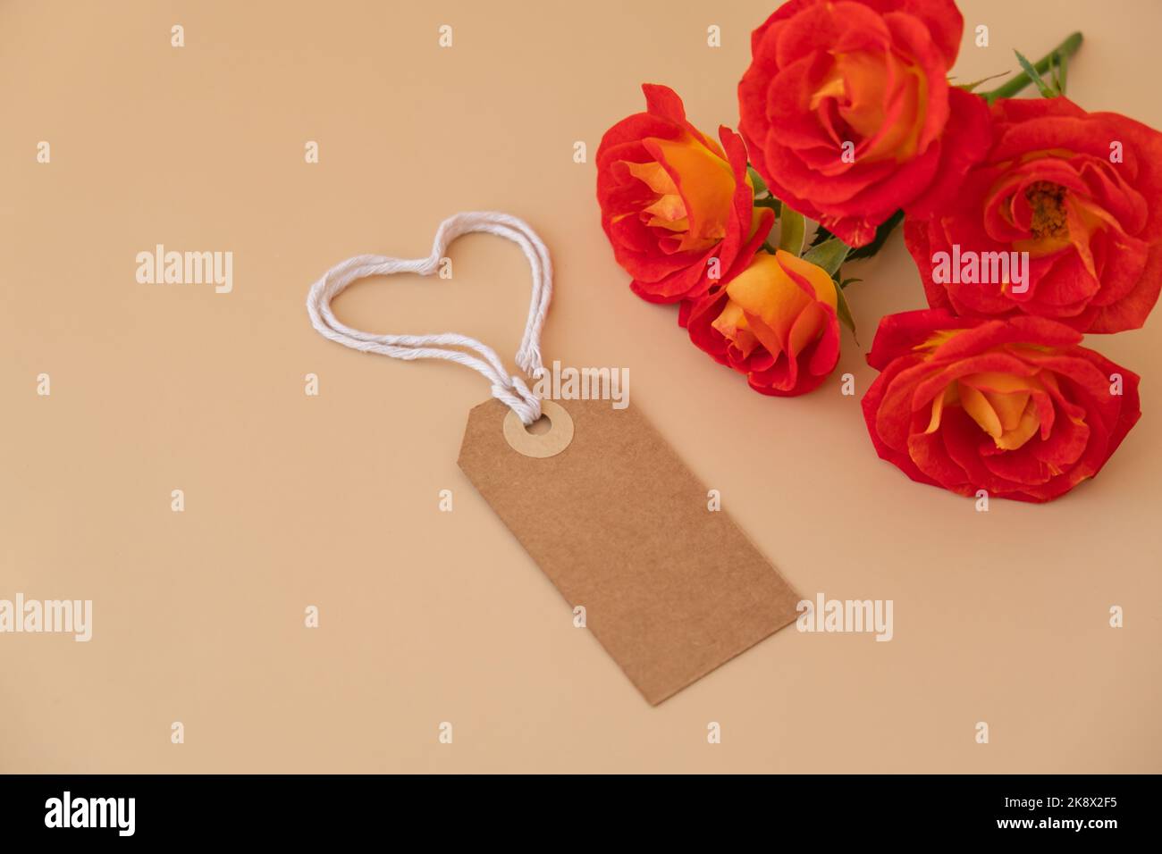 Einfarbige beige Papiernote und Seil in Herzform auf neutralem beigen Hintergrund. Zarte rote Rosen Grußkarte Feiertagsidee. Erstellen Sie einen Kopierplatz für Text. Geschenk Stockfoto