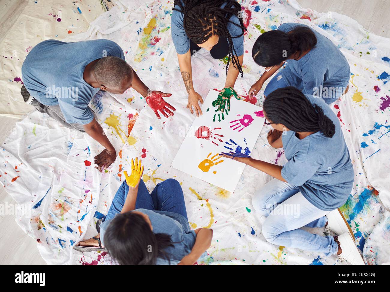 Werden Sie gemeinsam kreativ. Eine Gruppe von Menschen, die bemalte Handdrucke auf einem weißen Poster hinterlassen. Stockfoto