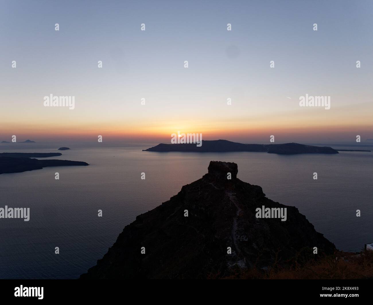 Skaros Rock Vordergrund, wenn die Sonne über Thirasia auf der griechischen ägäischen Kykladen Insel Santorin untergeht. Stockfoto