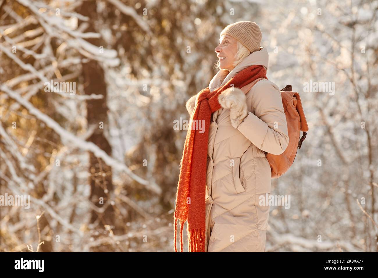 Seitenansicht Porträt einer lächelnden älteren Frau, die im von Sonnenlicht beleuchteten Winterwald wandern und Platz zum Kopieren genießen kann Stockfoto Seitenansicht Porträt einer lächelnden älteren Frau, die im von Sonnenlicht beleuchteten Winterwald wandern und Platz zum Kopieren genießen kann Stockfoto