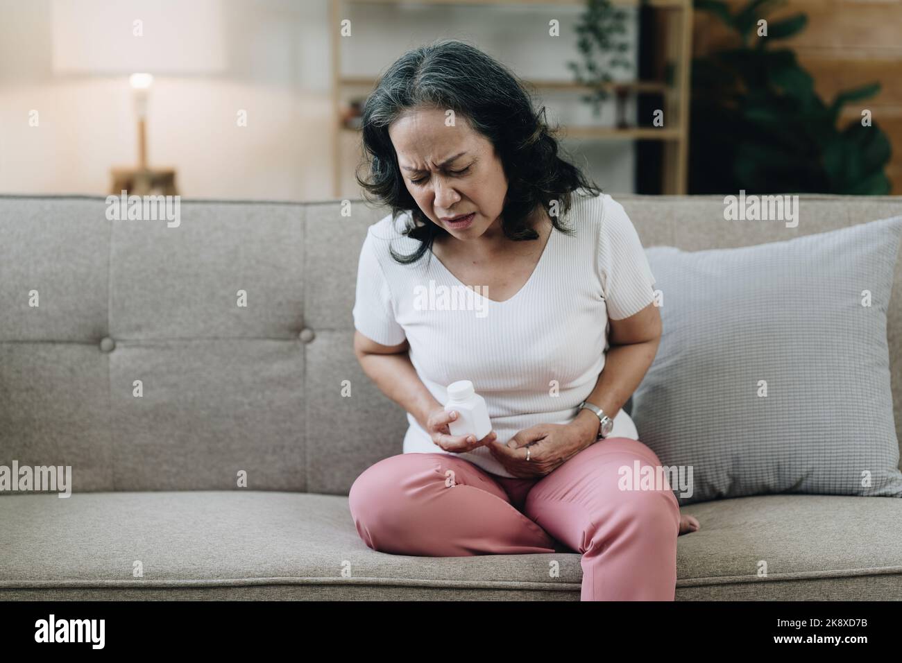 Die Asiatin in den Achtzigern, erschöpft und unter Stress, ist mit Magenschmerzen zu Hause Stockfoto