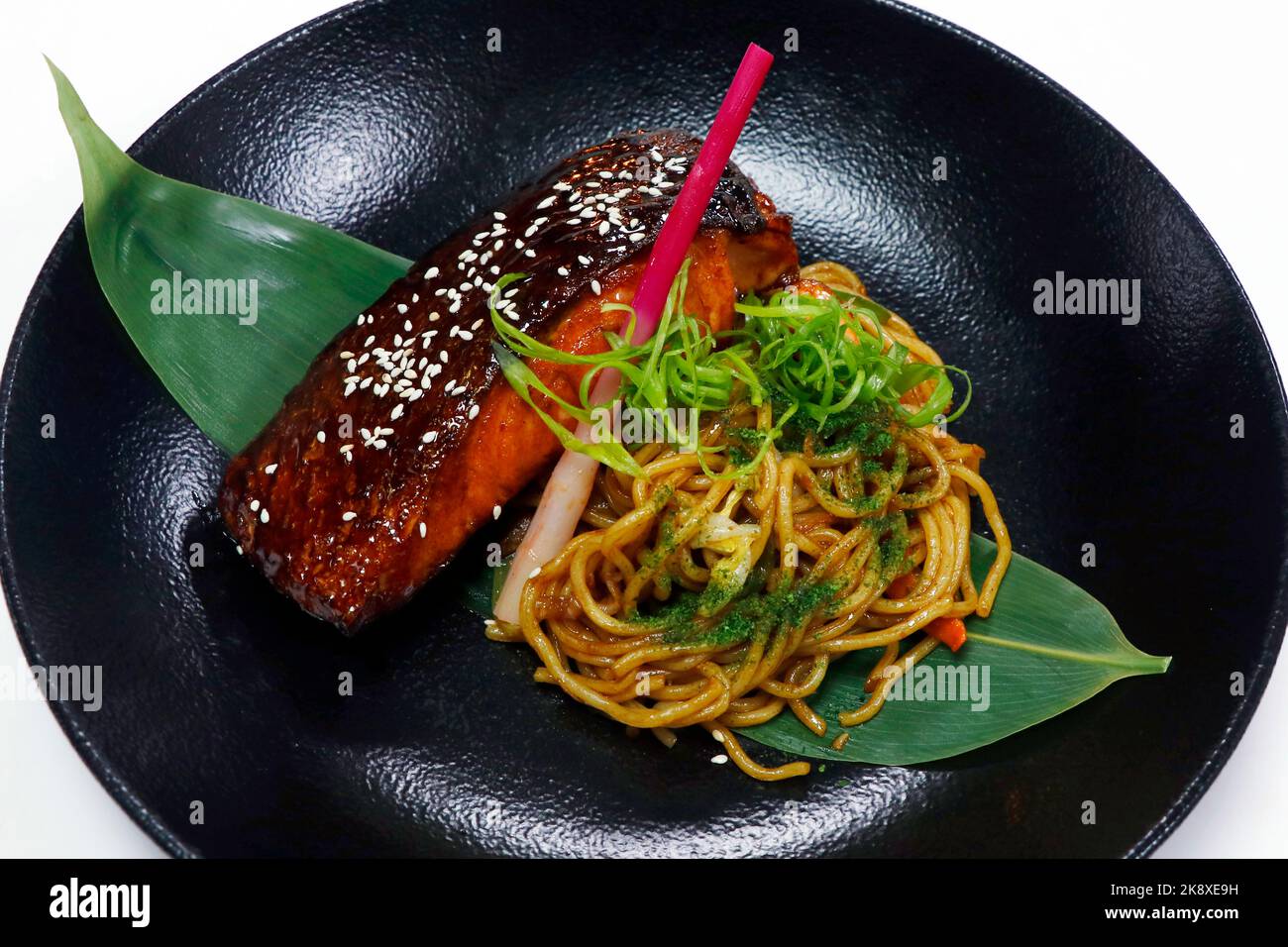 japanischer Teriyaki-Lachs mit gebratener Rührnudel und Ingwer schießt in einer schwarzen Schüssel mit weißem Hintergrund Stockfoto