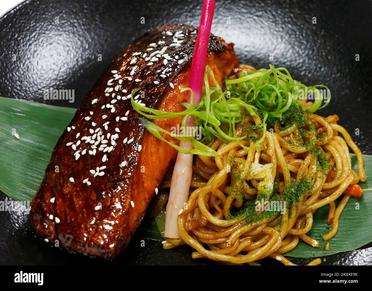 japanischer Teriyaki-Lachs mit gebratener Rührnudel und Ingwer schießt in einer schwarzen Schüssel mit Nahaufnahme Stockfoto